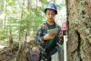 Emily Dewald-Wang holds a PVC pipe which is the target for the laser survey tool (total station). She calls out the species, size, and condition. The data are recorded into a tablet and then the tree's location is mapped with the total station laser.